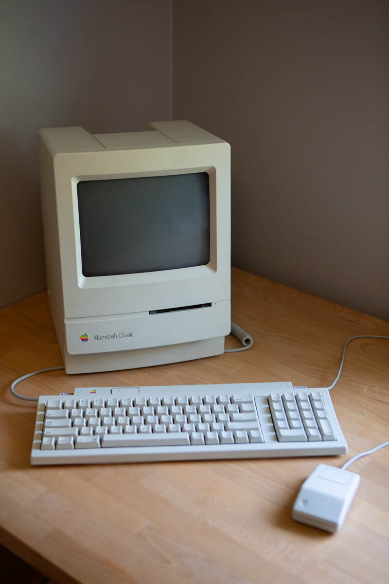 A fully restored beige Macintosh Classic on a wooden desk