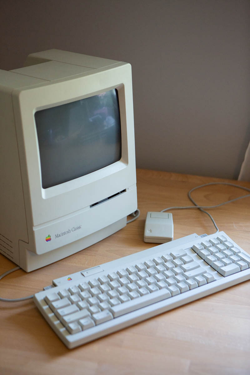 The restored Macintosh Classic with its beige keyboard and mouse on a wooden desk