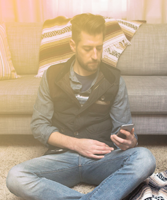 Photo of Steve sitting on the floor in front of a couch, looking at a phone.